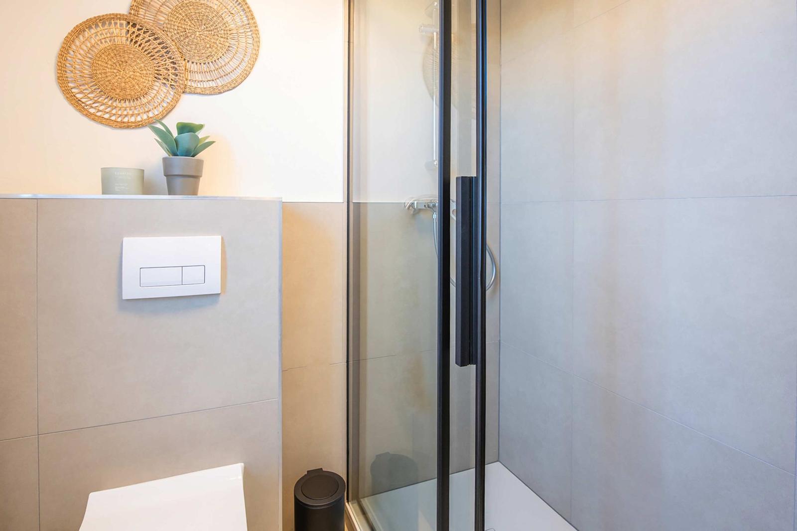 Shower with glass enclosure, toilet, and wall decor