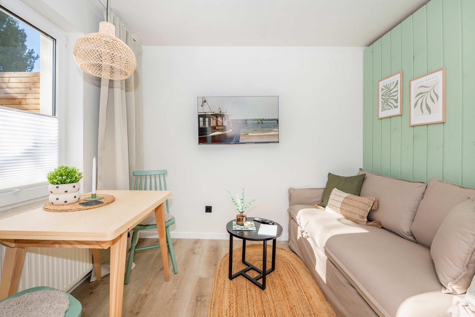 Living room with sofa, table, chair, and wall picture. Green wall paneling and window with blinds.