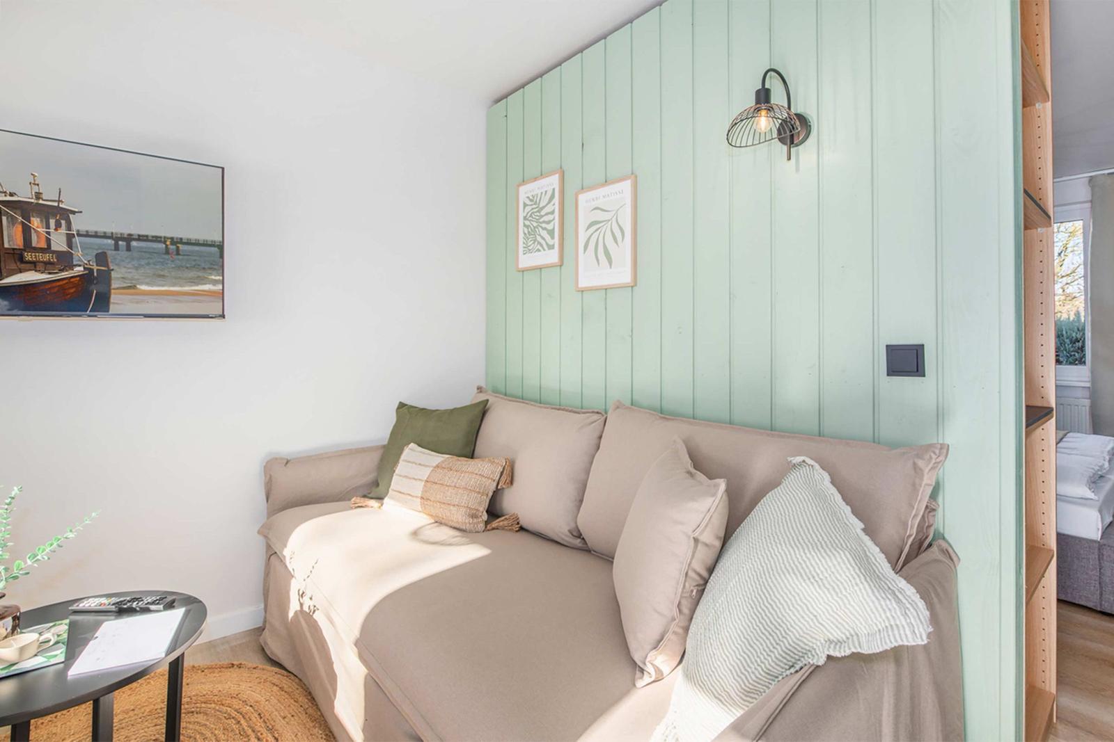 Sofa with cushions in front of mint-colored wooden wall and wall lamp.