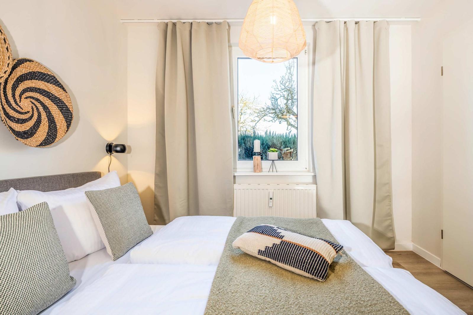 Bedroom with bed, window, and curtains. On the bed are pillows and a blanket.