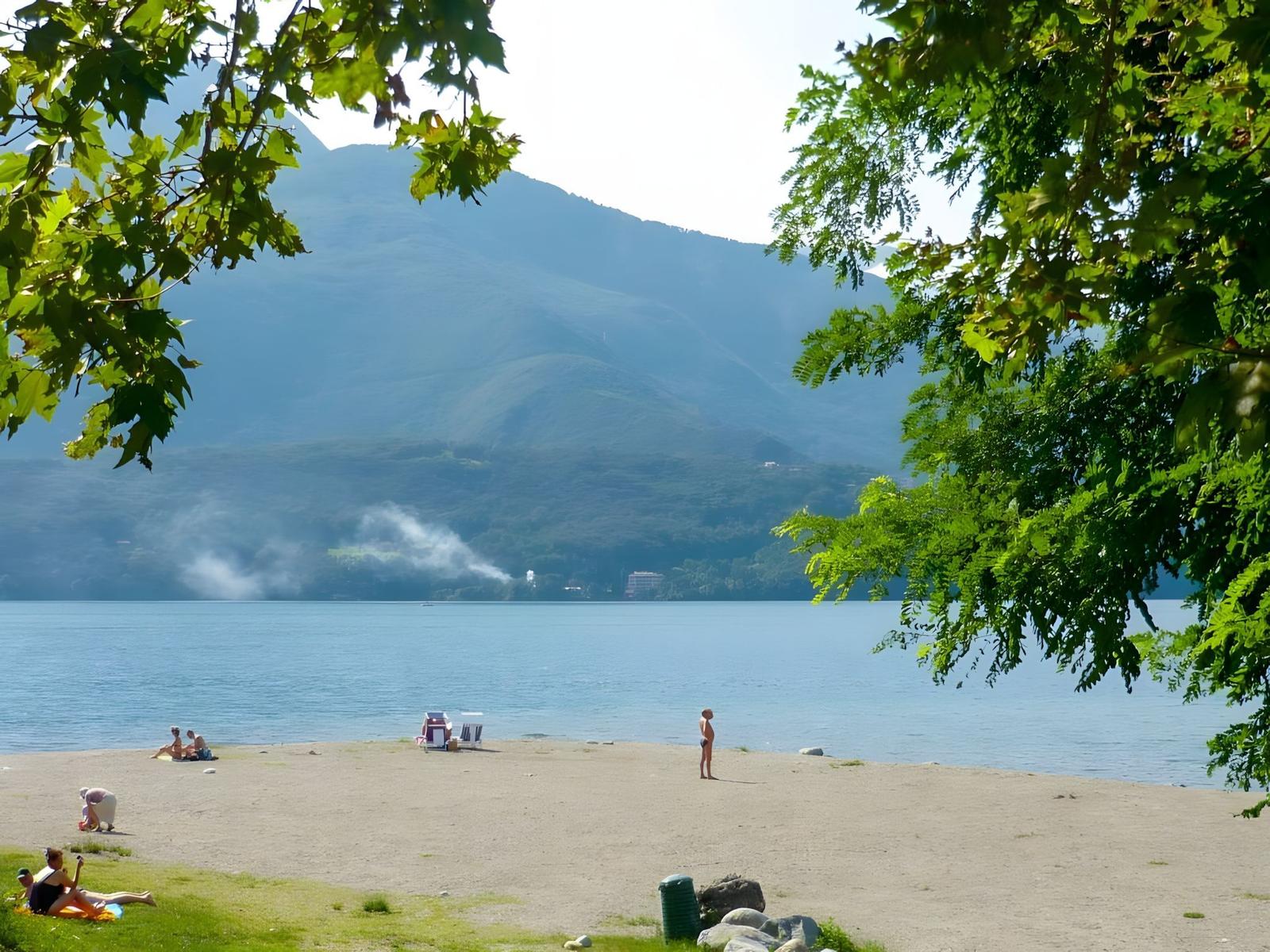 Strand mit Menschen, See und Bergen im Hintergrund