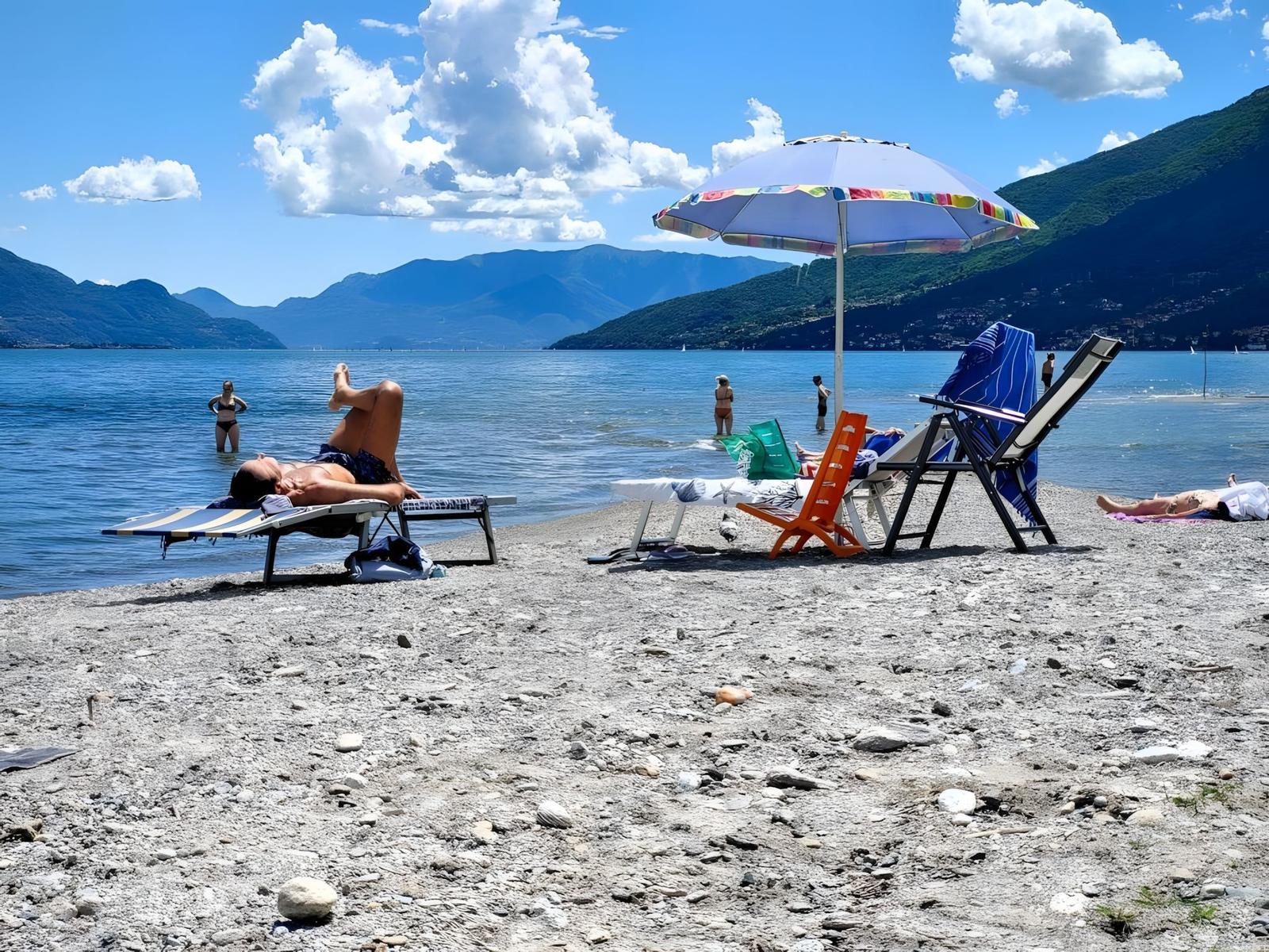 Strand mit Liegestühlen und Sonnenschirm am See. Menschen baden und sonnen sich.