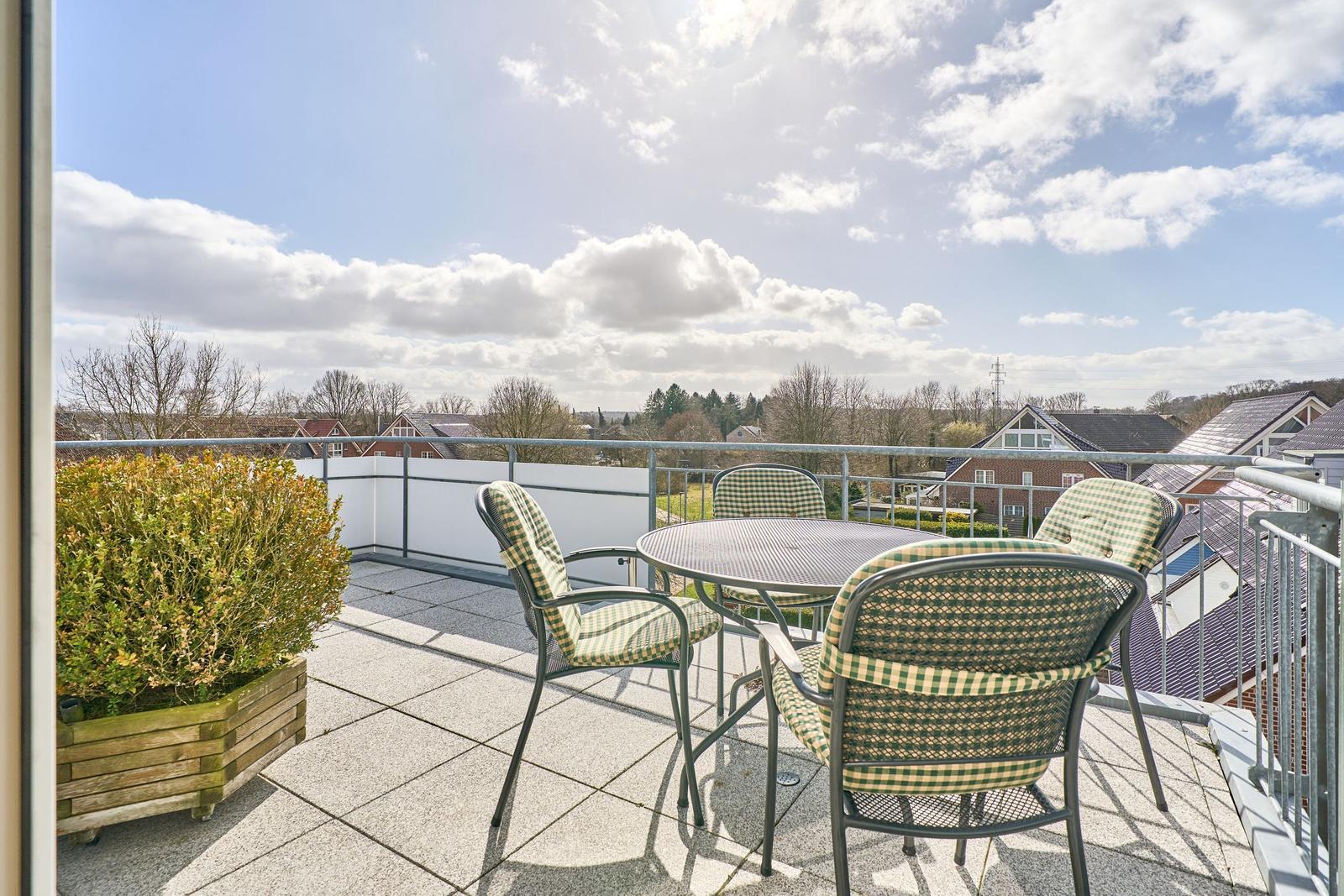 Terrasse mit Tisch und Stühlen, Blick auf Wohnhäuser und Bäume unter blauem Himmel.