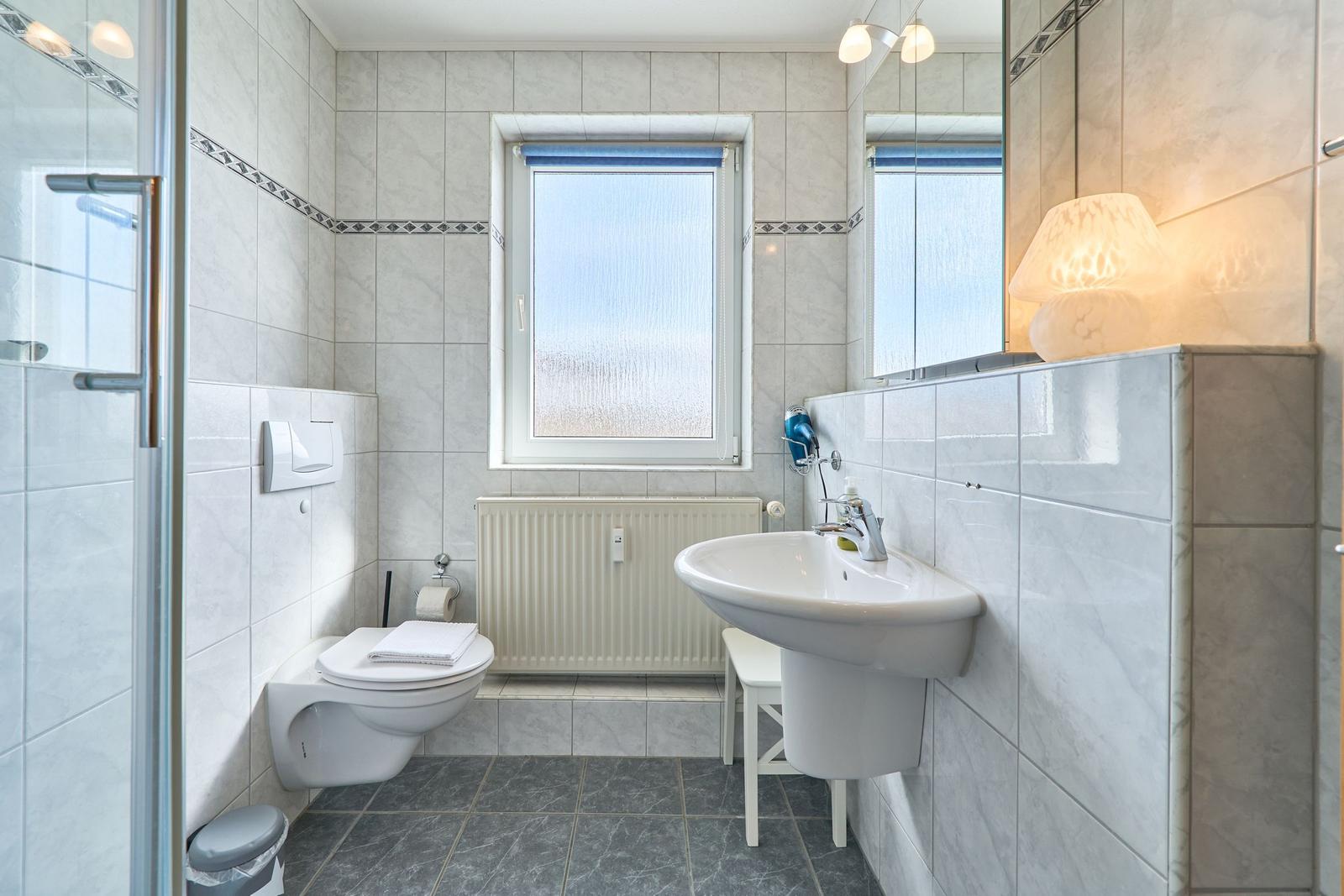 Badezimmer mit Dusche, Toilette, Waschbecken und Fenster.