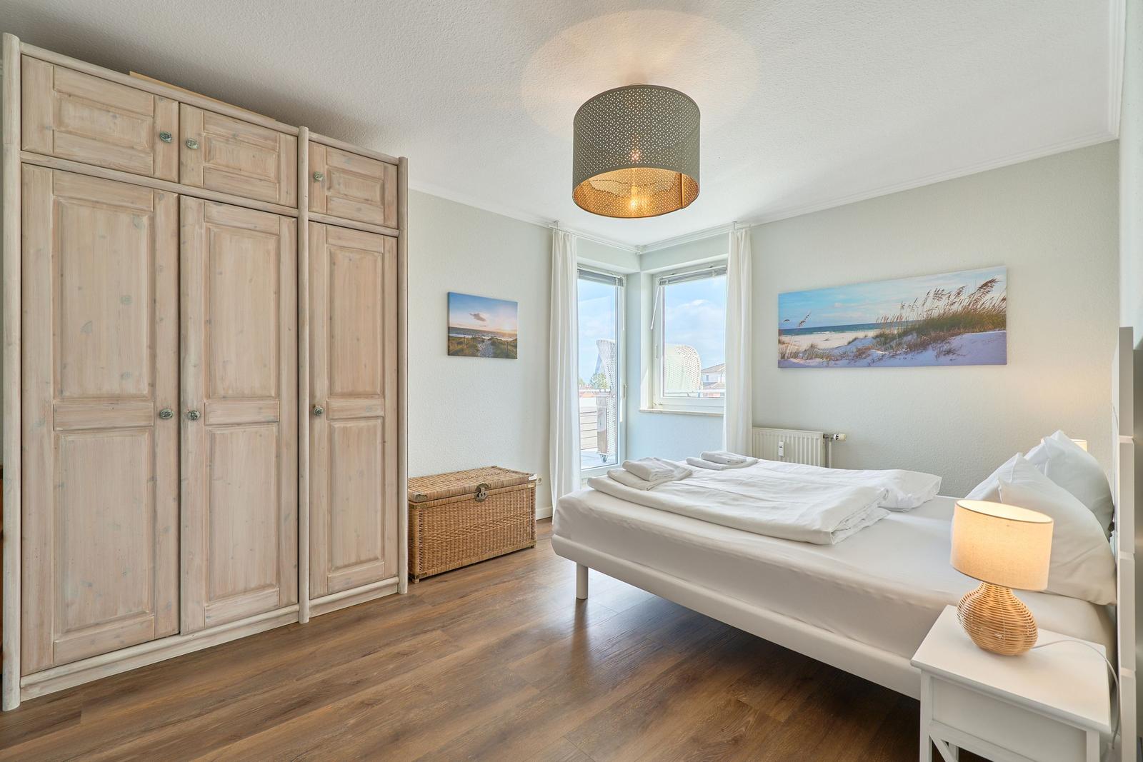 Schlafzimmer mit Bett, Kleiderschrank und Fenster zum Balkon.