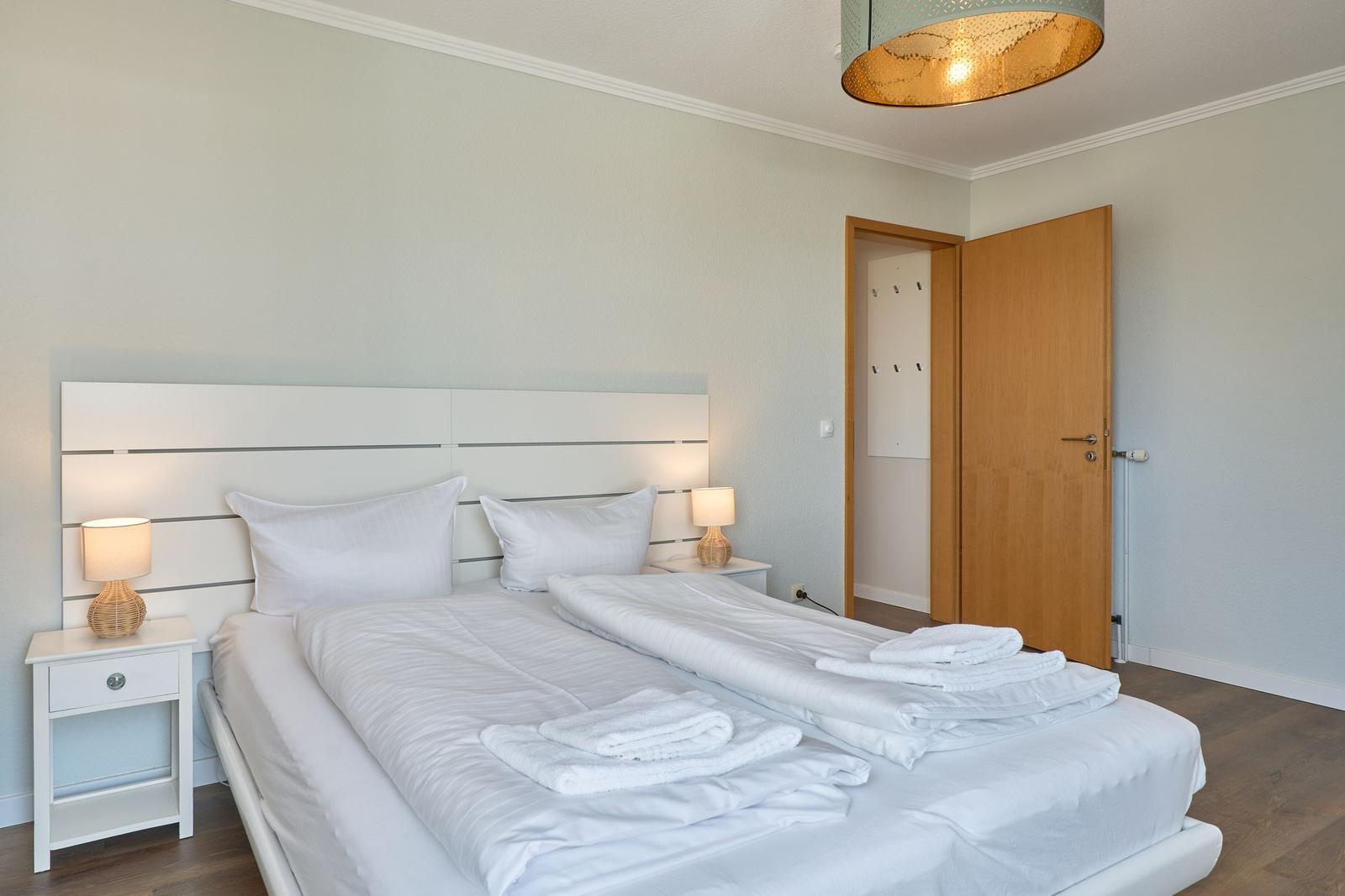 Schlafzimmer mit Doppelbett, zwei Nachttischen und einer Tür zum Ankleidebereich.