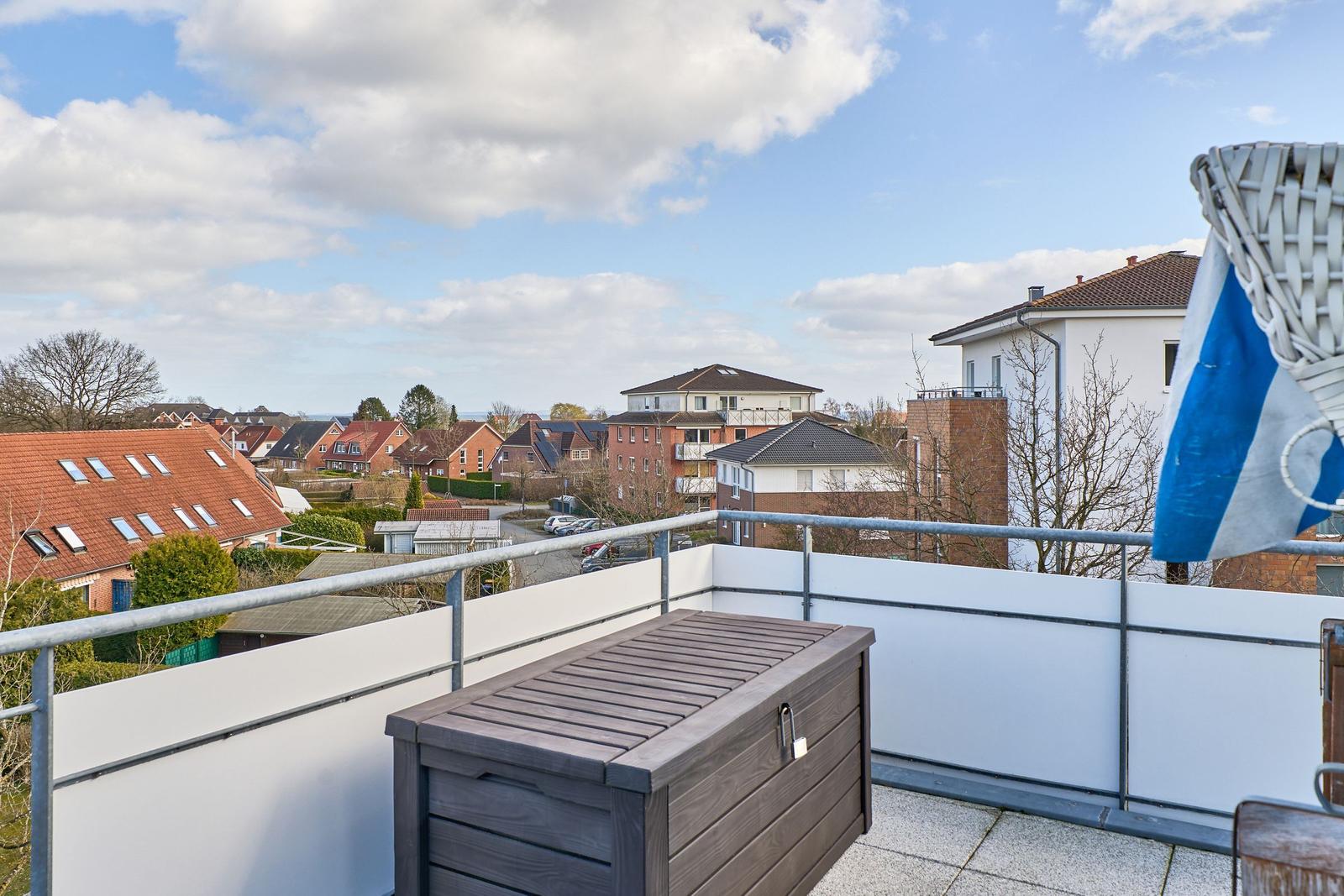 Terrasse mit Blick auf Wohnhäuser und Himmel. Holzbox und weißer Geländer.