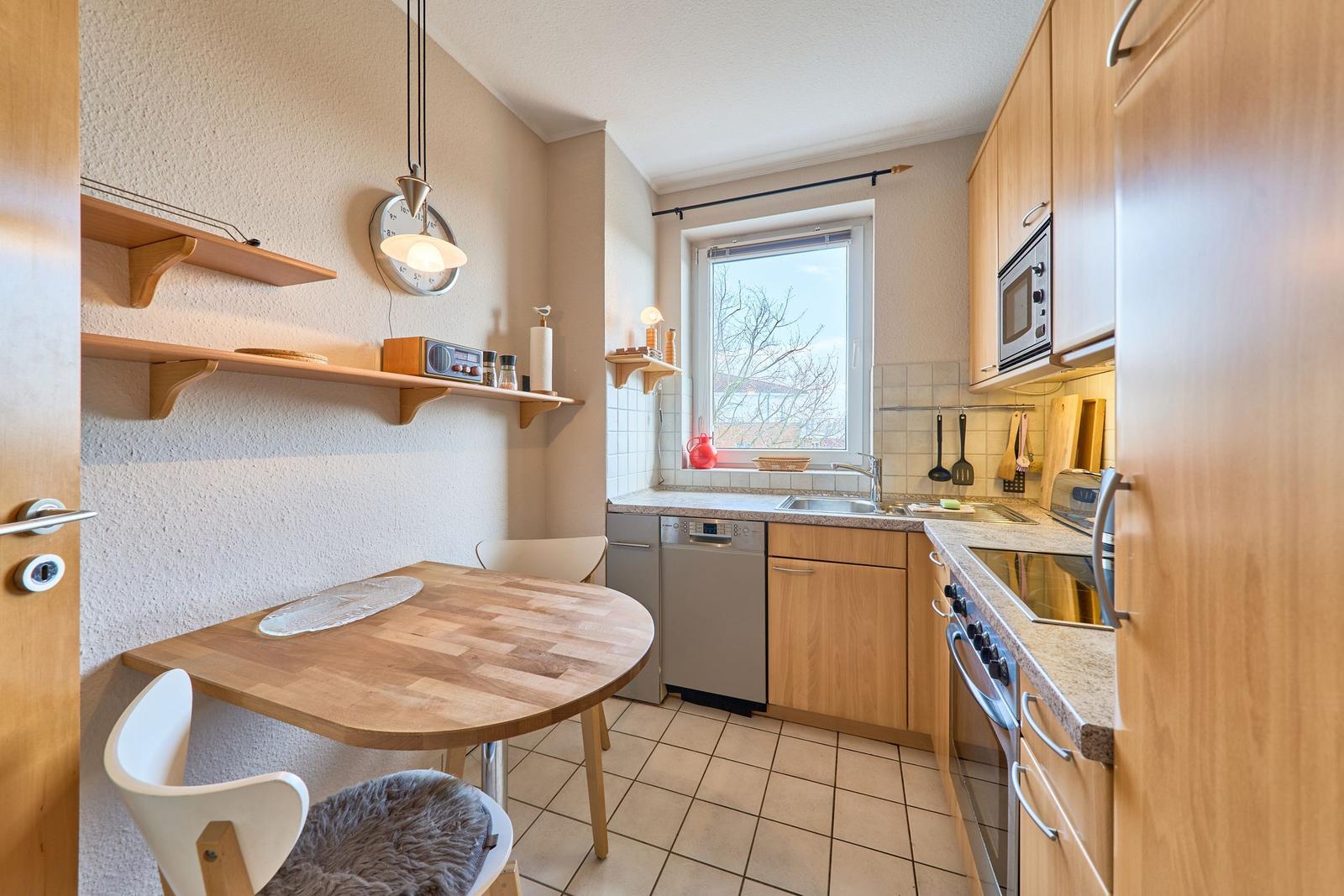 Küche mit Essbereich, Holztisch, Spüle und Fenster.