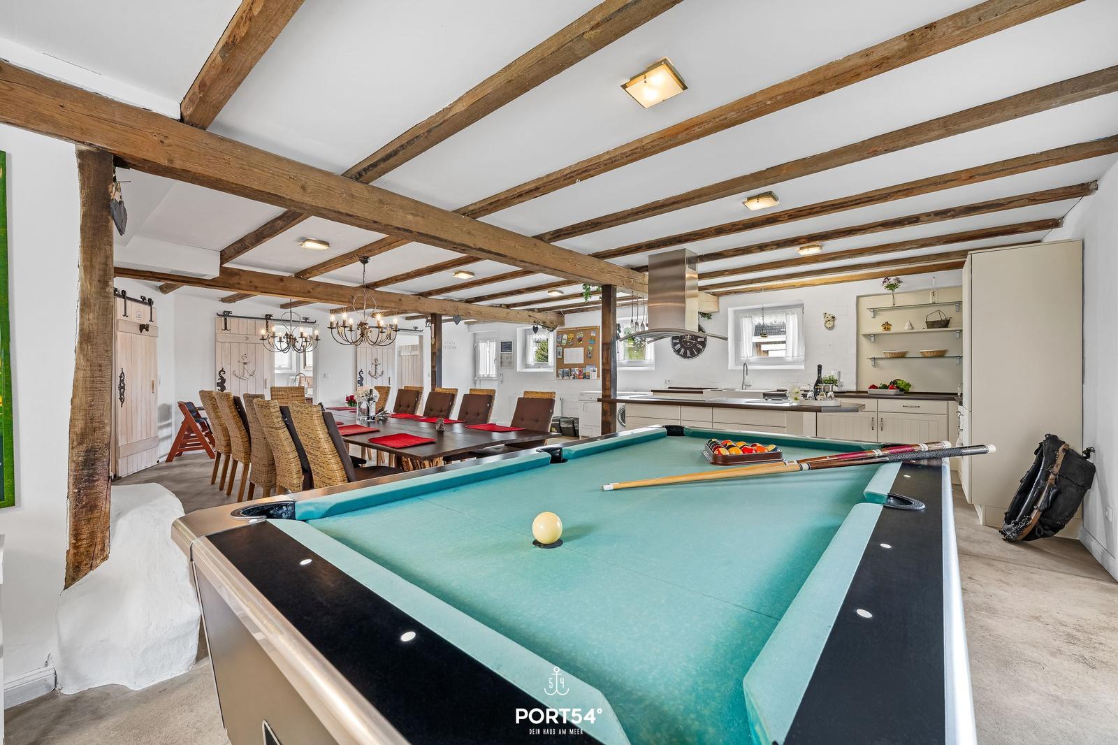 Pooltisch im Vordergrund, dahinter Essbereich und Küche mit Holzbalkendecke.