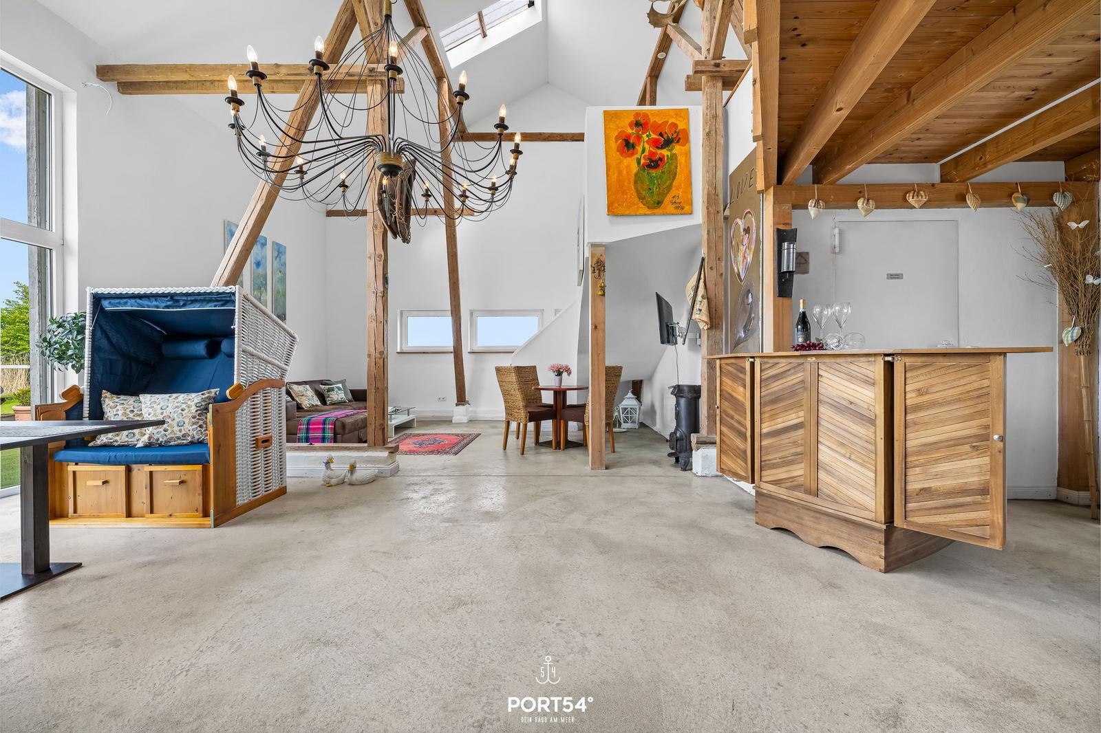 Großer Raum mit Holzkonstruktion, Bar und Sitzgelegenheiten. Helle Wände und hohe Decke.