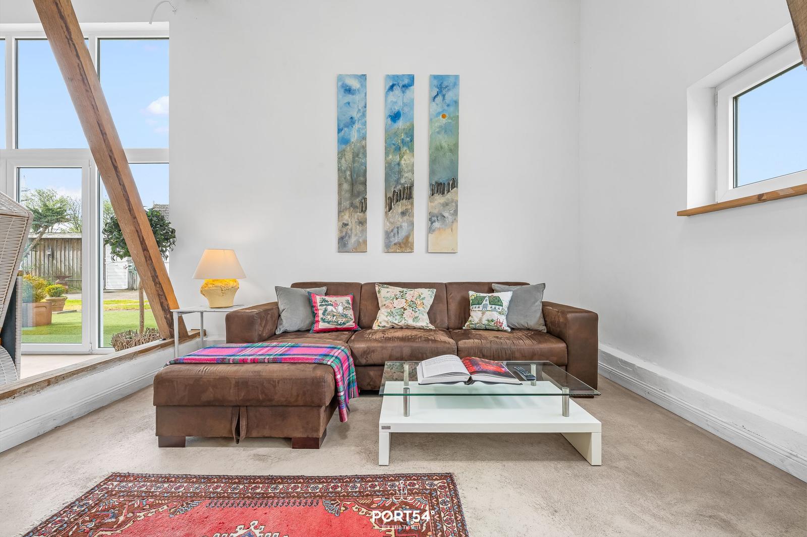 Wohnzimmer mit braunem Sofa, Glas-Tisch und Fenster zur Außenseite.