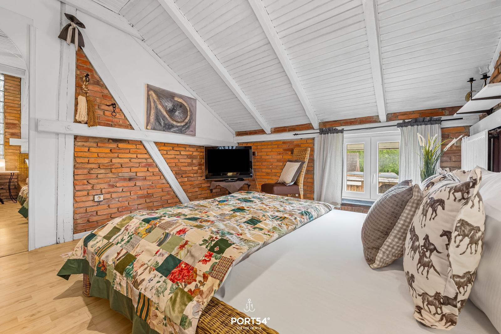 Schlafzimmer mit Dachschrägen, Backsteinwand und Bett mit Kissen.