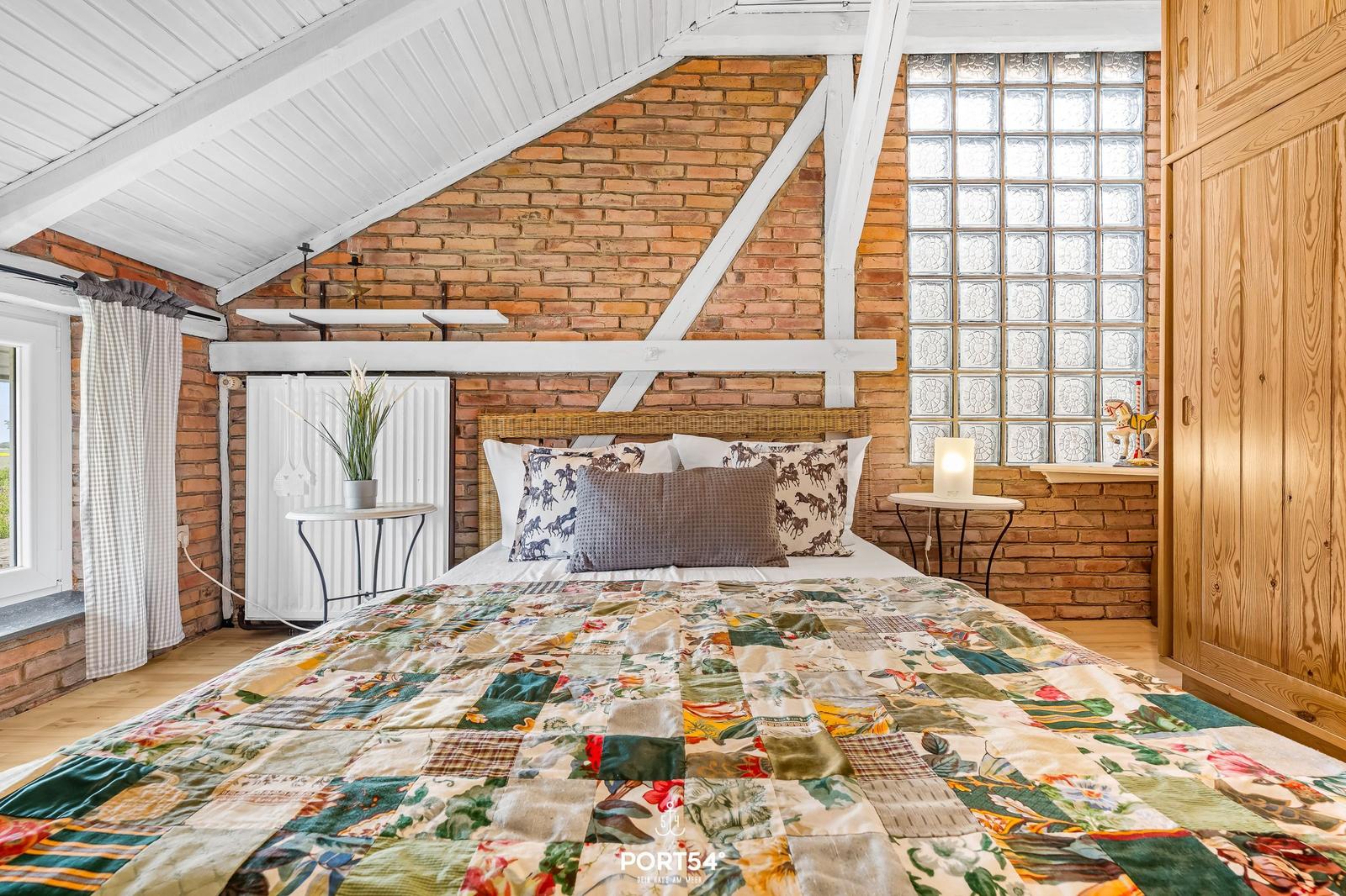 Schlafzimmer mit gemütlichem Bett, Backsteinwand und Glasblöcken.