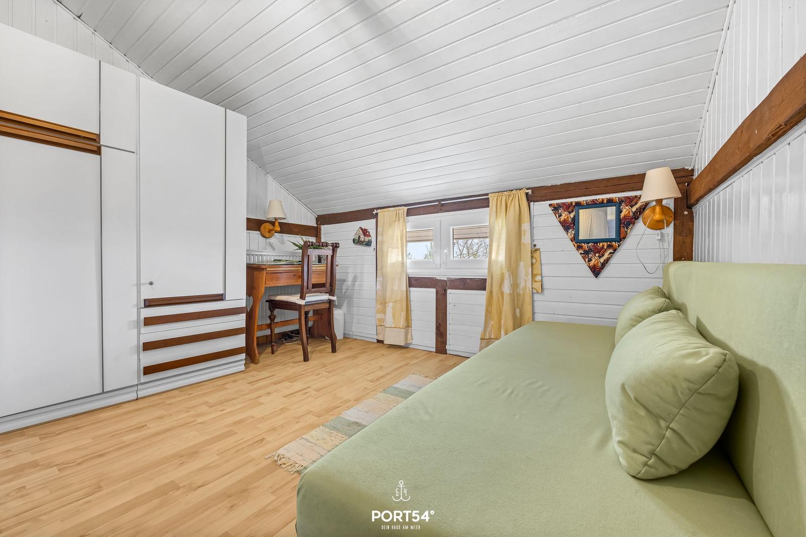 Ein Schlafzimmer mit grünem Sofa, Schreibtisch und weißen Schränken.