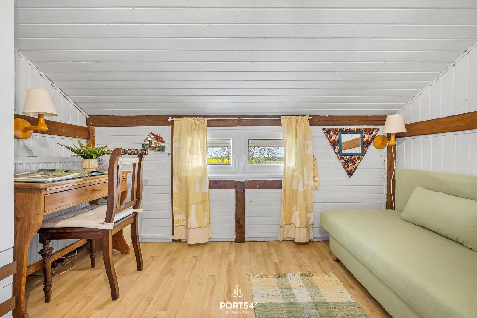 Raum mit Schreibtisch, Sofa und Fenster mit Vorhängen.