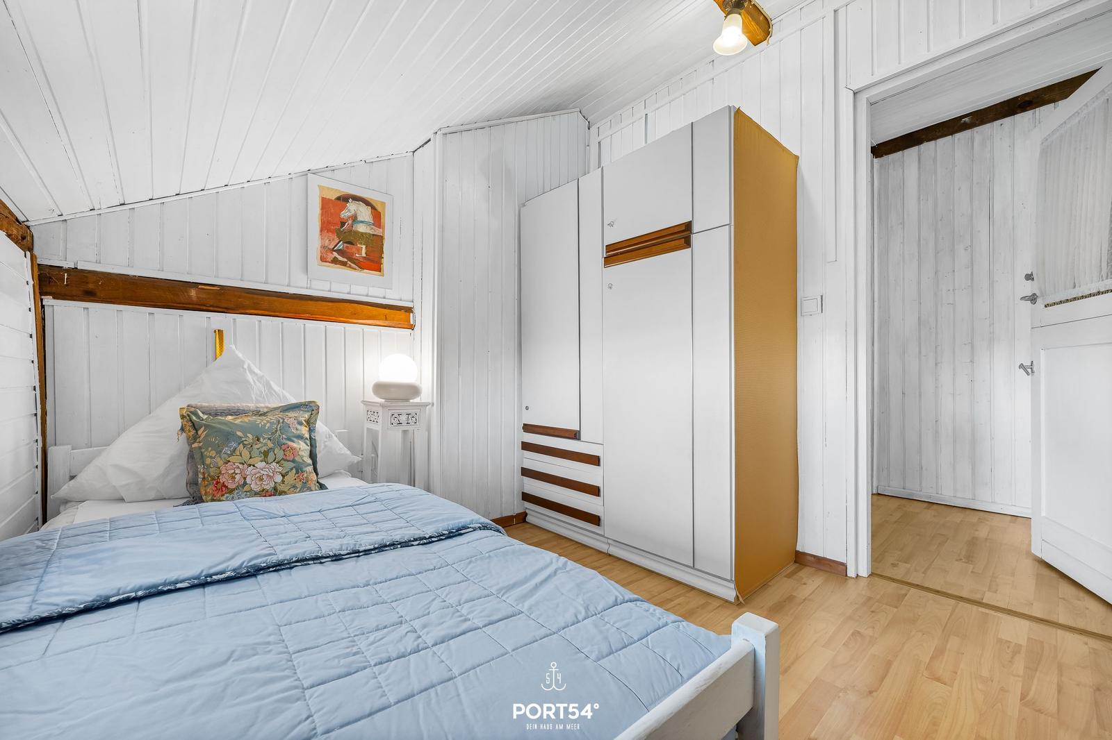 Schlafzimmer mit Bett, Kleiderschrank und Holzboden.