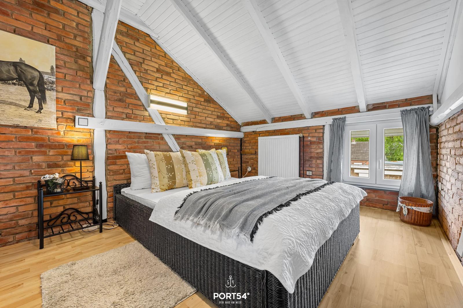 Schlafzimmer mit Dachschräge, Ziegelwand, Bett und Fenster.