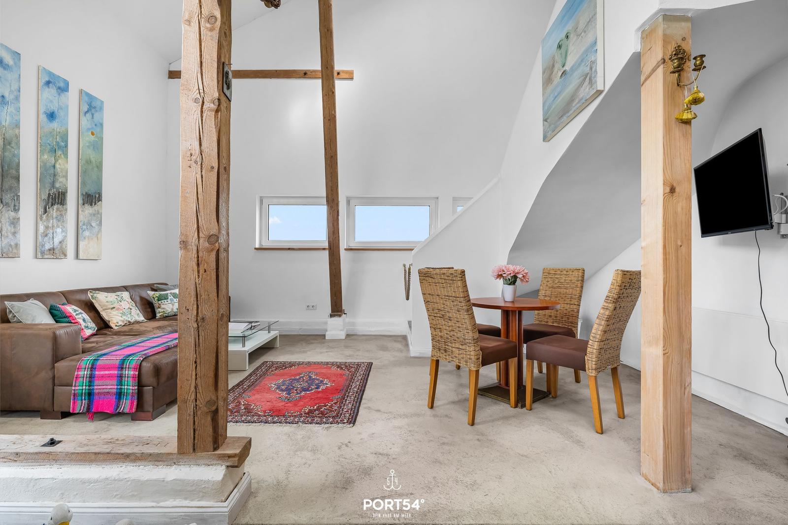Wohn- und Essbereich mit Sofa, Tisch, Stühlen und Holzsäulen.