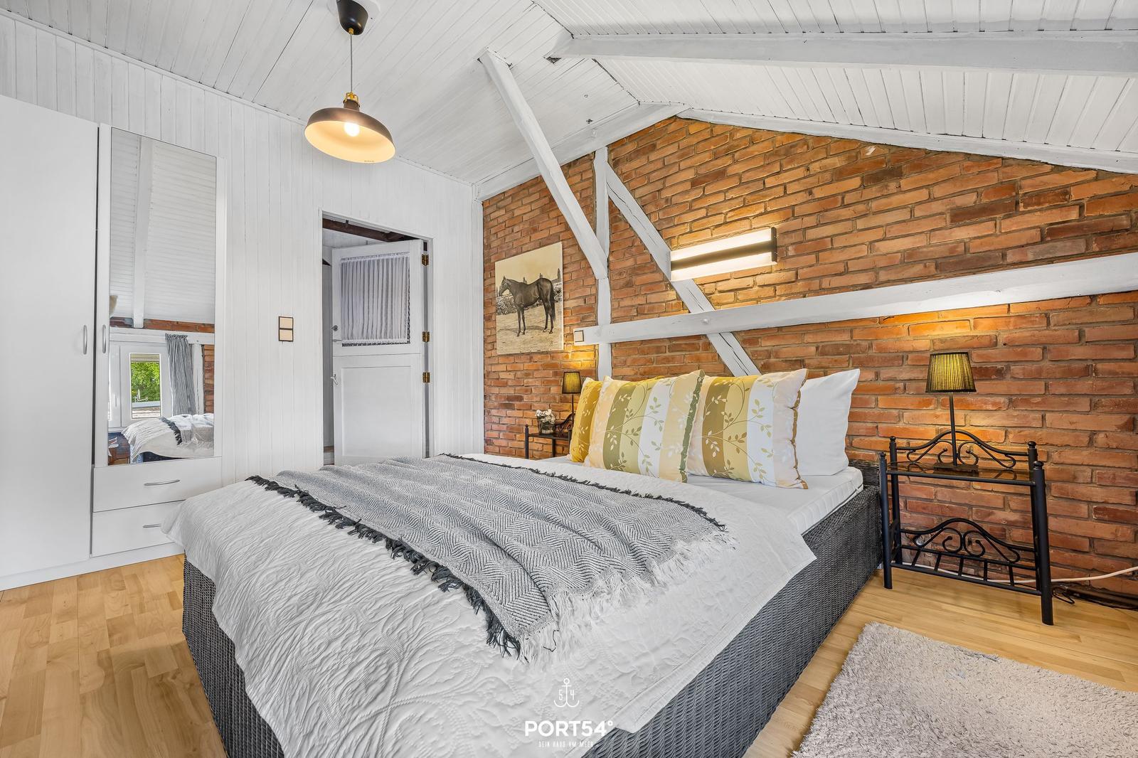 Schlafzimmer mit Bett, Wandbild und Holzboden. Zwei Nachttische und Spiegelschrank.