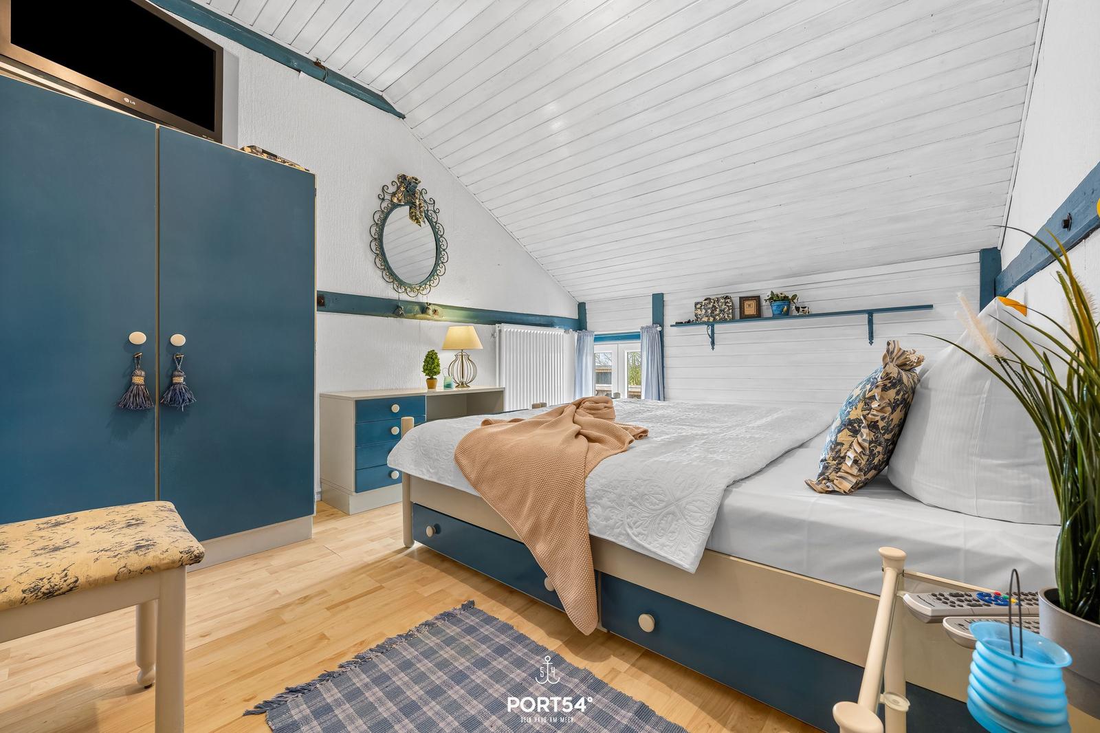 Schlafzimmer mit Bett, Kleiderschrank und Fernseher unter schrägem Dach.