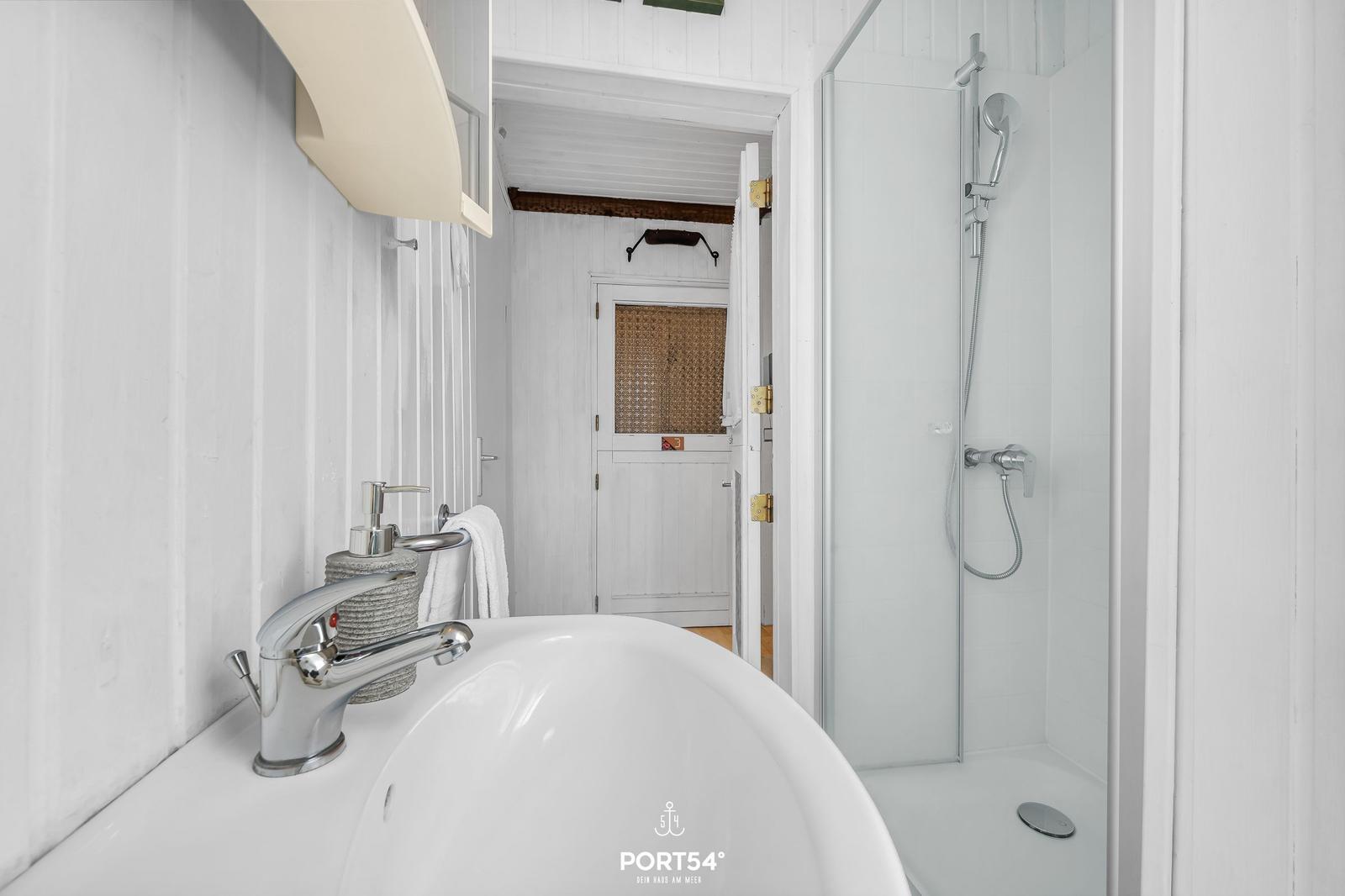 Badezimmer mit Dusche und Waschbecken. Weiße Wände und moderne Armaturen.