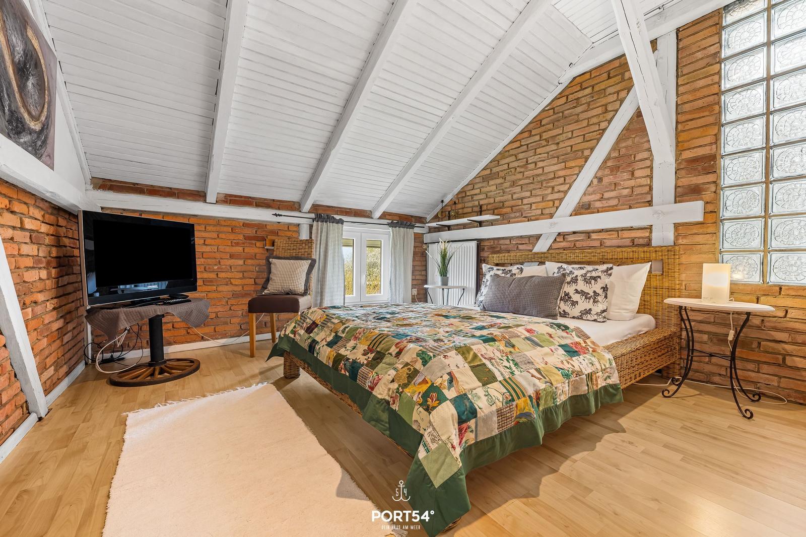 Schlafzimmer mit Dachschräge, Ziegelwand, Bett und Fernseher.