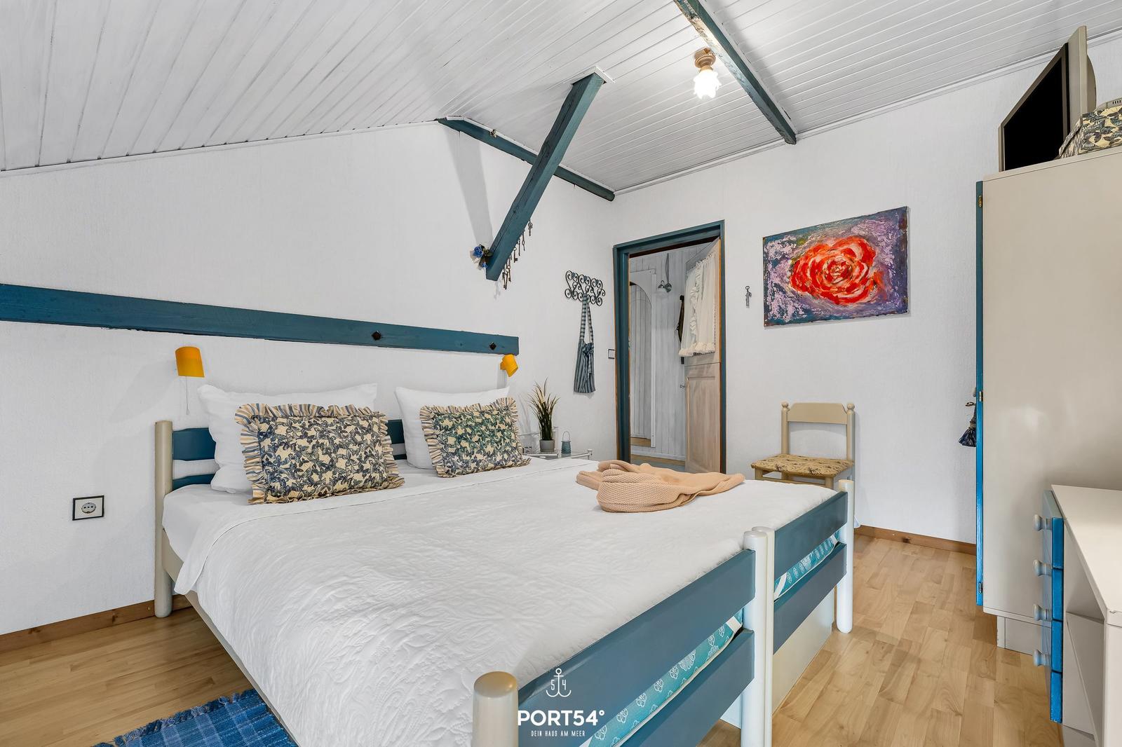 Schlafzimmer mit Doppelbett, blauer Kopf- und Fußteil, Wandbild und Holzboden.