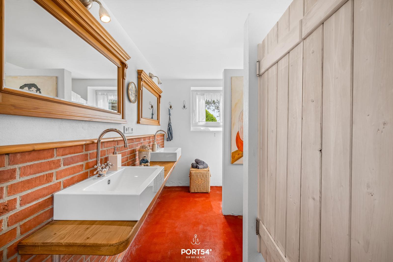 Badezimmer mit Waschbecken, Spiegel und rotem Boden