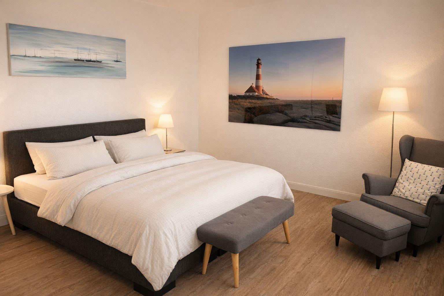Schlafzimmer mit Bett, Sessel und Wandbildern von Leuchtturm und Schiffen.