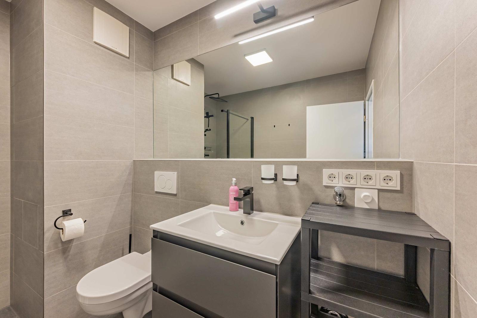 Badezimmer mit Waschbecken, Spiegel, Toilette und Dusche