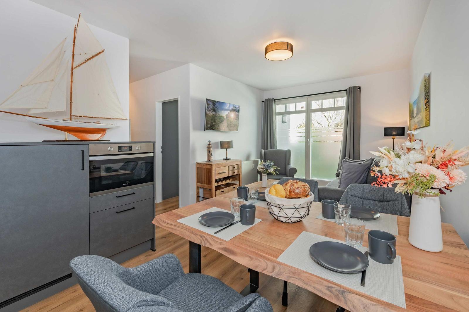 Esszimmer mit Holztisch, Stühlen und Küchenzeile. Dekoration mit Blumen und Segelschiffmodell.