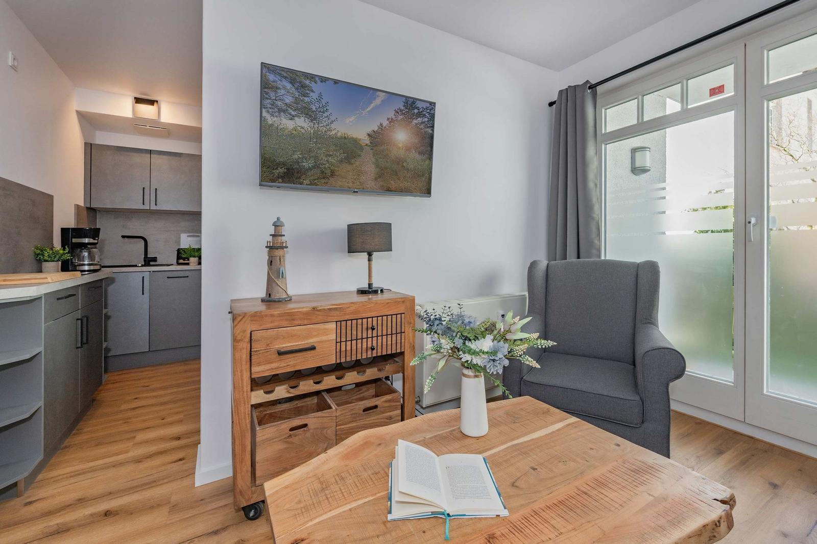 Wohnzimmer mit TV, Sessel und Küchenbereich im Hintergrund.