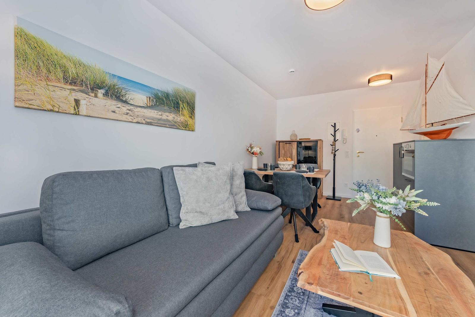 Wohnzimmer mit Sofa, Esstisch und Küchenzeile. Wandbild und Segelschiffmodell sind sichtbar.