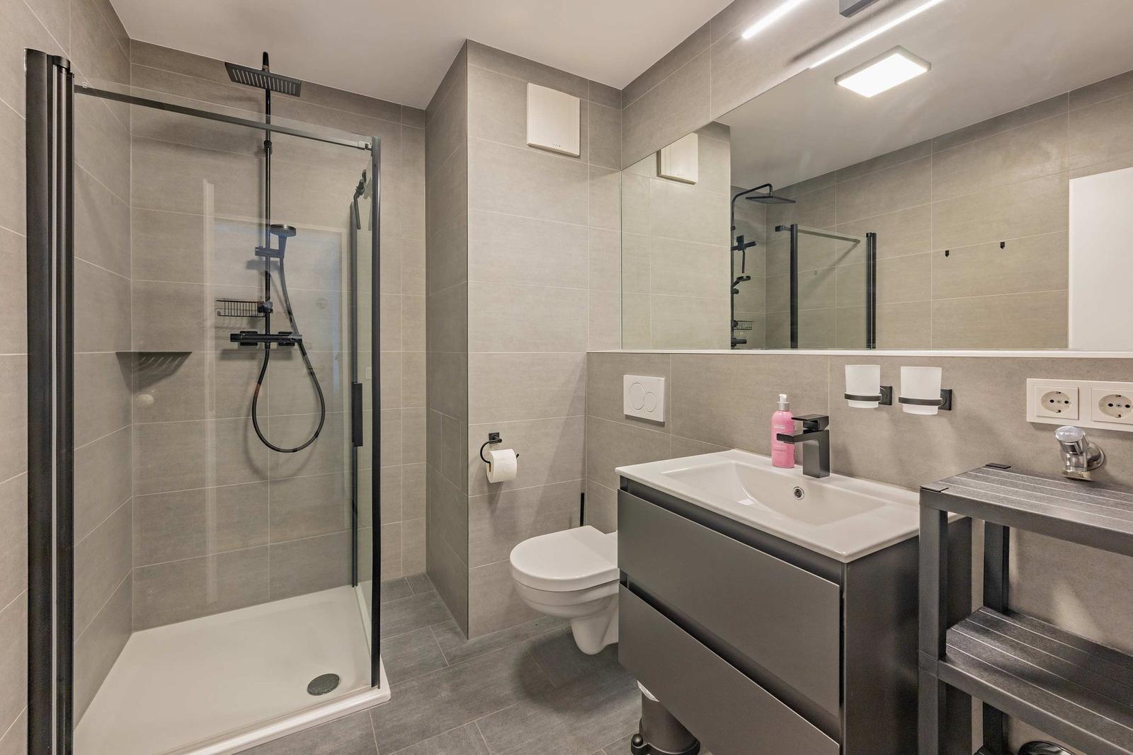 Badezimmer mit Dusche, Waschbecken und Toilette. Fliesen und moderne Einrichtung.