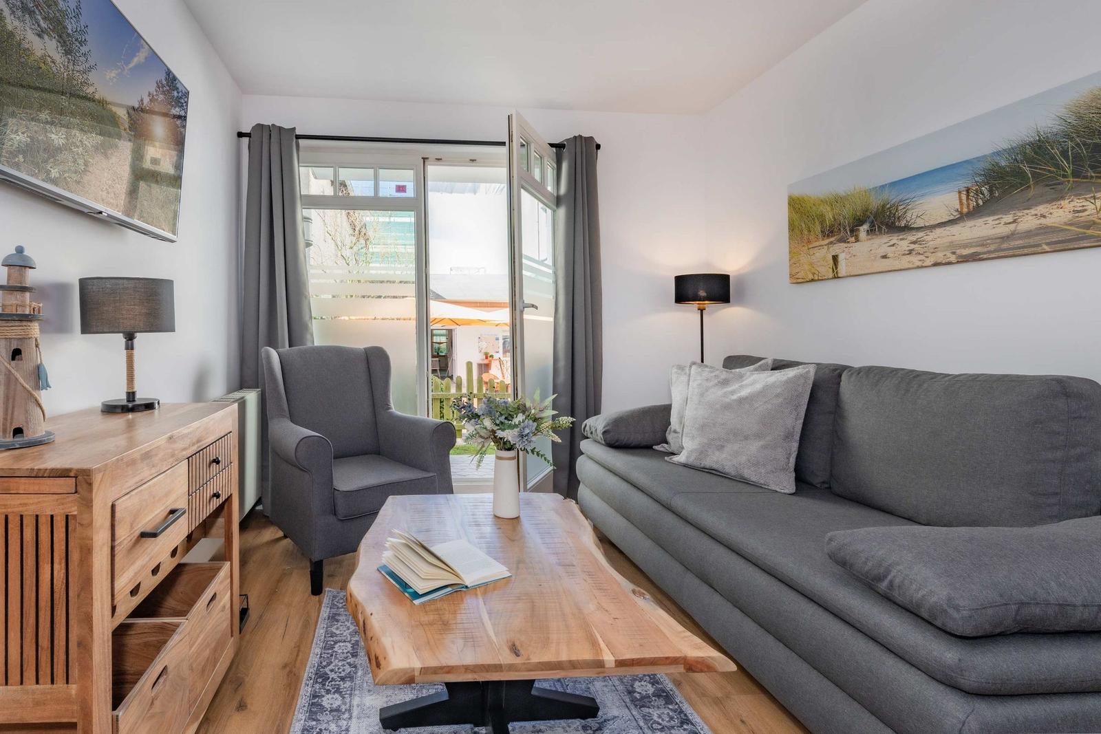 Wohnzimmer mit Sofa, Sessel, Holztisch und Fenster zur Terrasse.