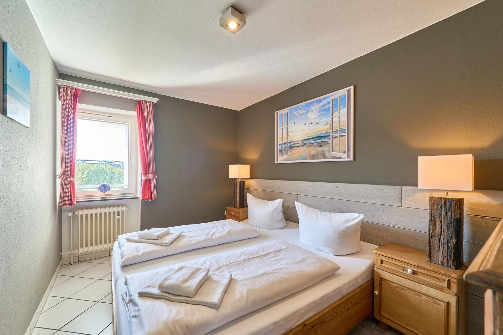 Schlafzimmer mit Doppelbett, zwei Nachttischen und Fenster mit roten Vorhängen.