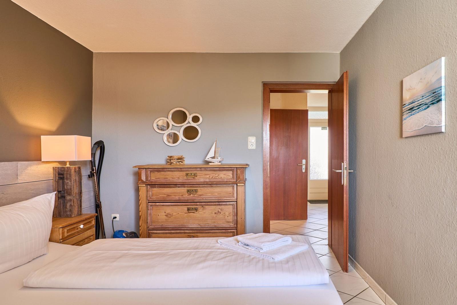 Schlafzimmer mit Bett, Schrank und Wandbild. Tür führt in angrenzenden Raum.