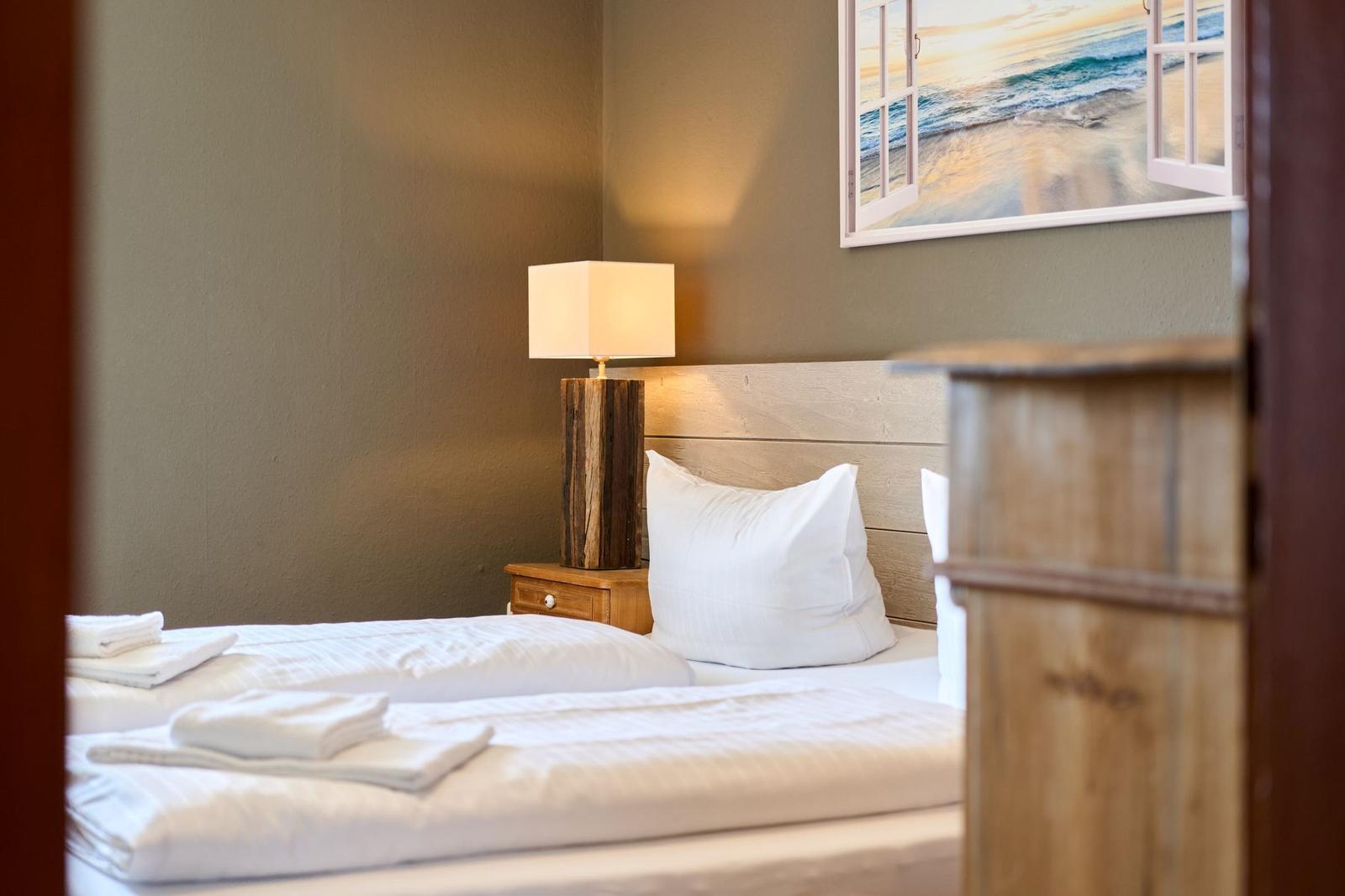 Schlafzimmer mit Bett, Nachttisch und Wandbild. Holzgestell und weiße Bettwäsche.