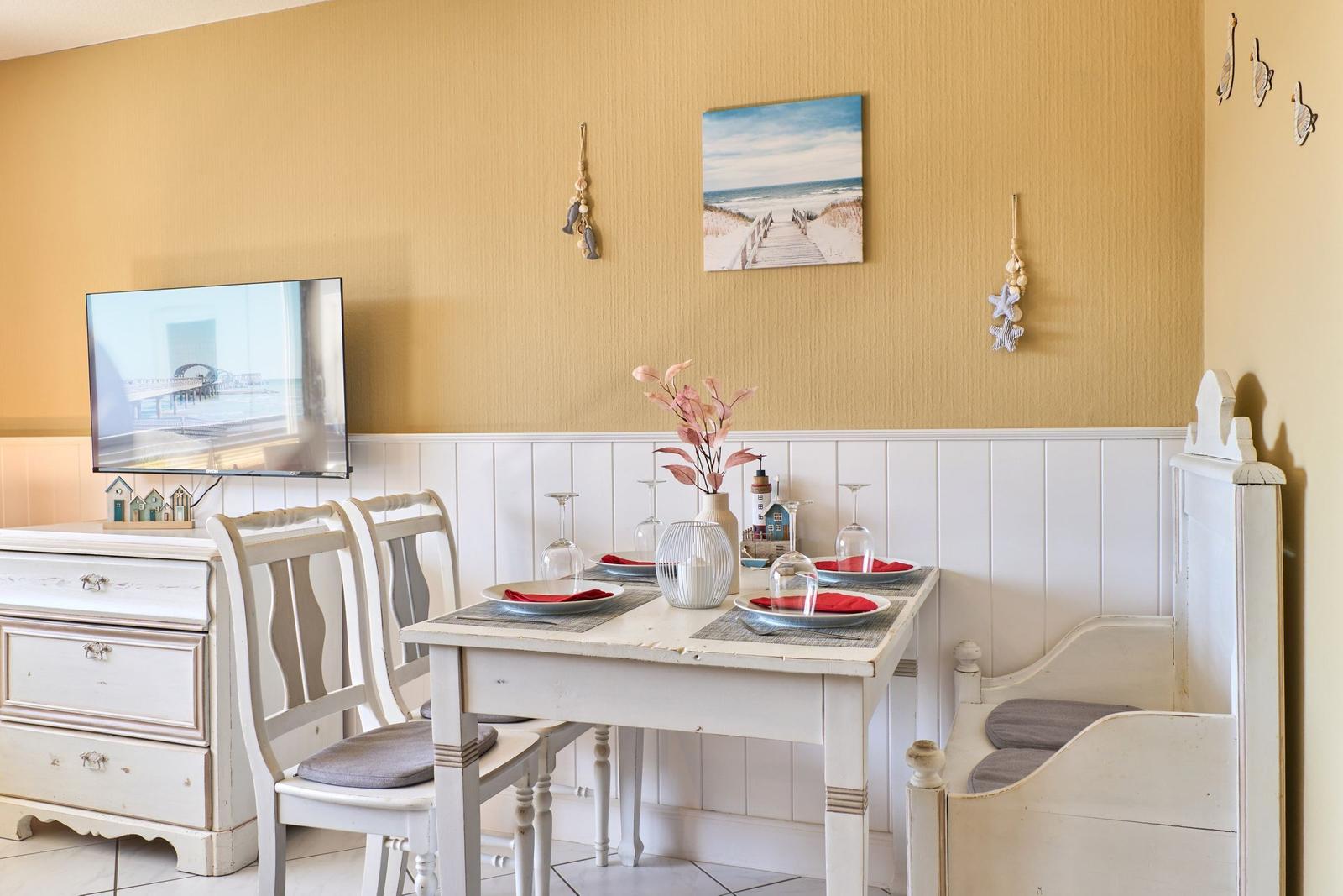 Esszimmer mit weißem Tisch, Stühlen und Bank. Wandbild und Dekorationen an der Wand.