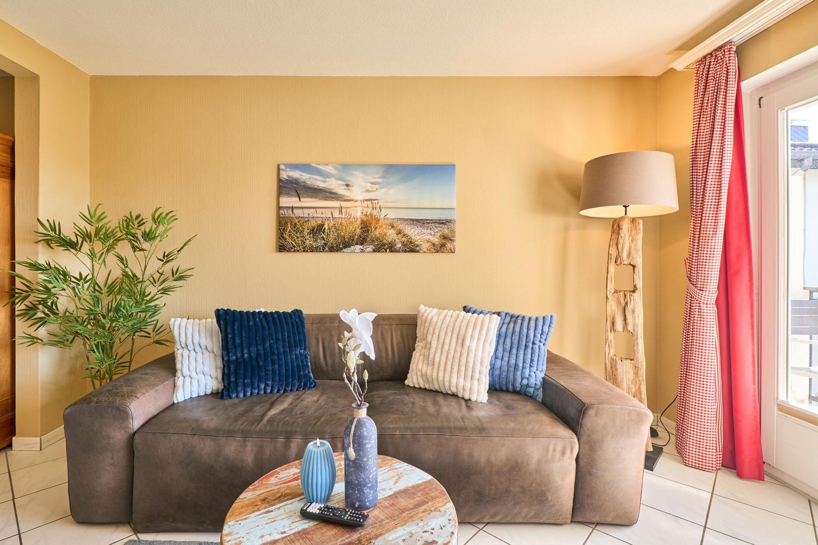 Ein Wohnzimmer mit braunem Sofa, Kissen und einem runden Tisch. An der Wand hängt ein Bild.