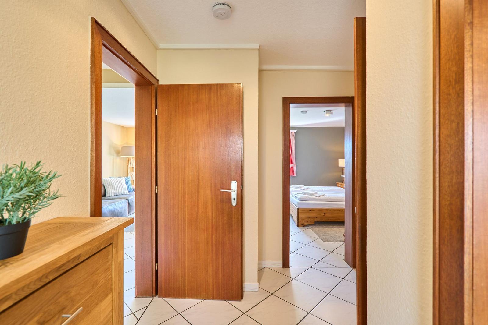 Flur mit Holztüren, Blick in Schlafzimmer und Wohnzimmer. Bodenfliesen, Pflanze auf Schrank.