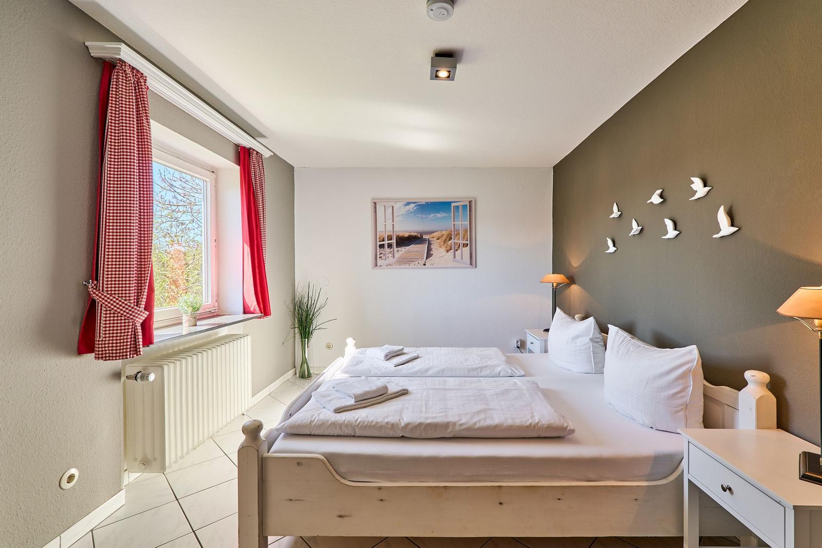 Schlafzimmer mit Doppelbett, Fenster und Wanddekoration.