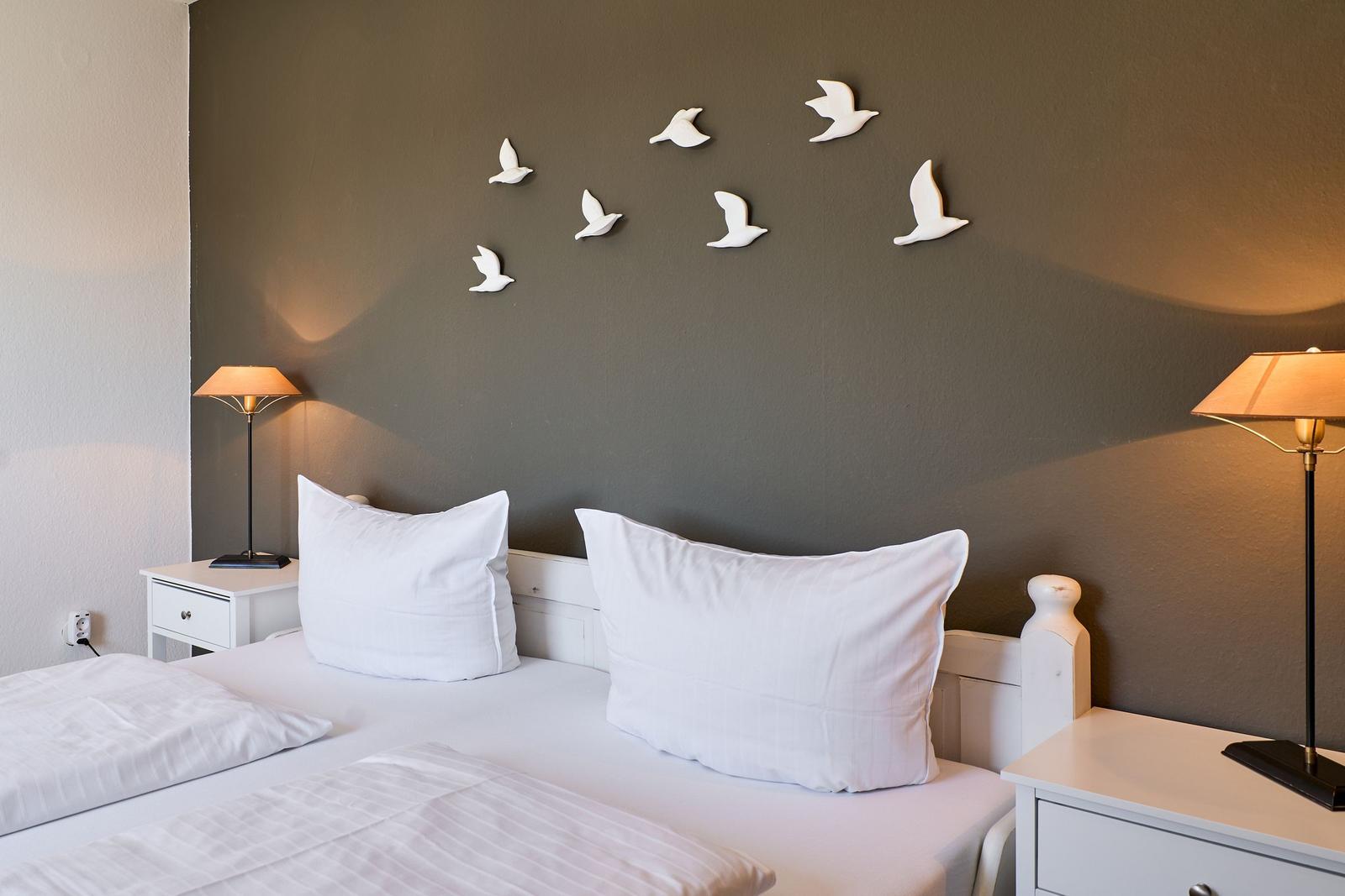 Schlafzimmer mit Bett, Nachttischen und Wanddekoration aus weißen Vögeln.