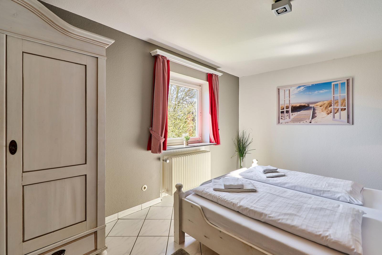 Schlafzimmer mit Bett, Kleiderschrank und Fenster mit roten Vorhängen.