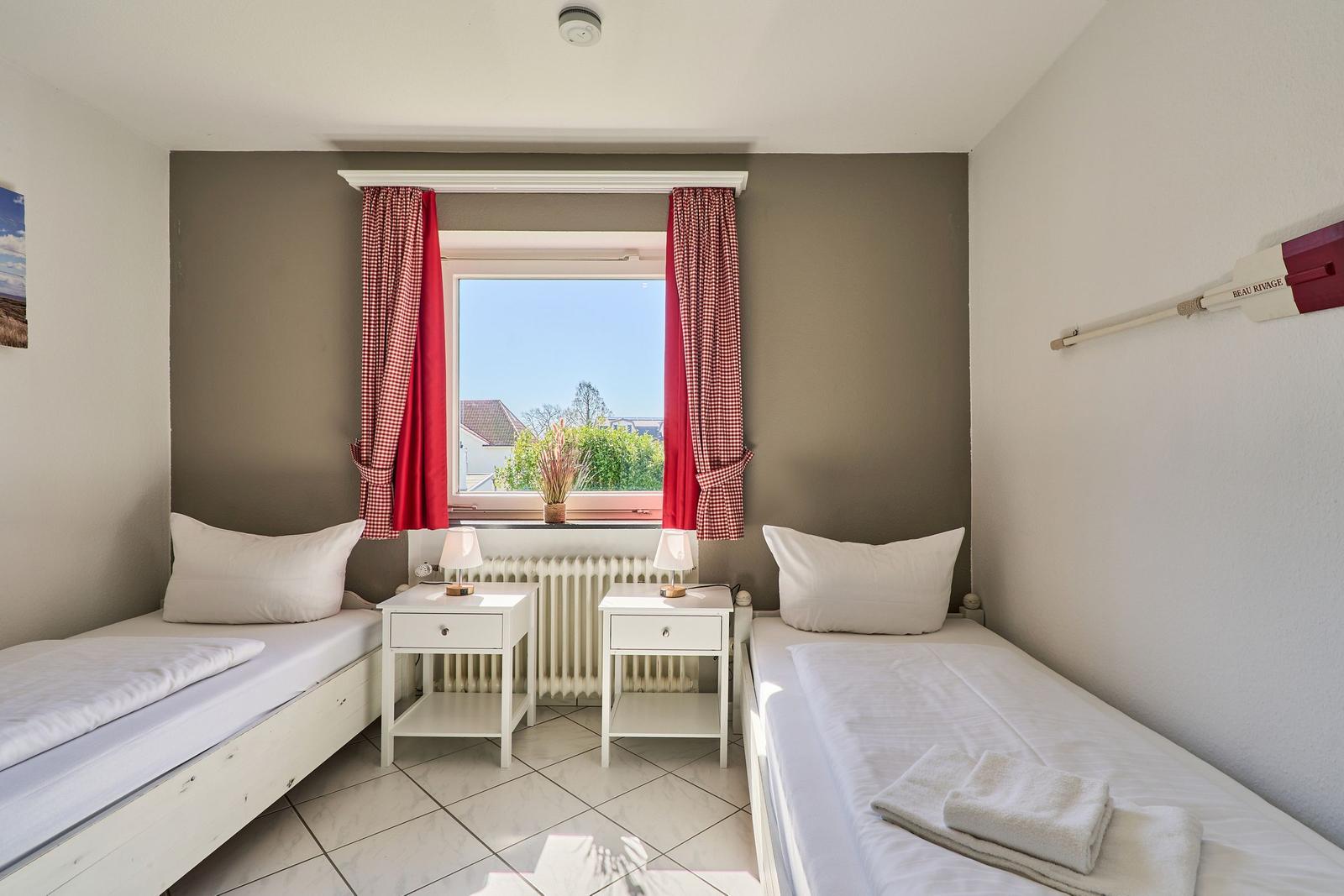 Zwei Betten mit weißen Bettwäsche, Fenster mit roten Vorhängen und zwei Nachttische.