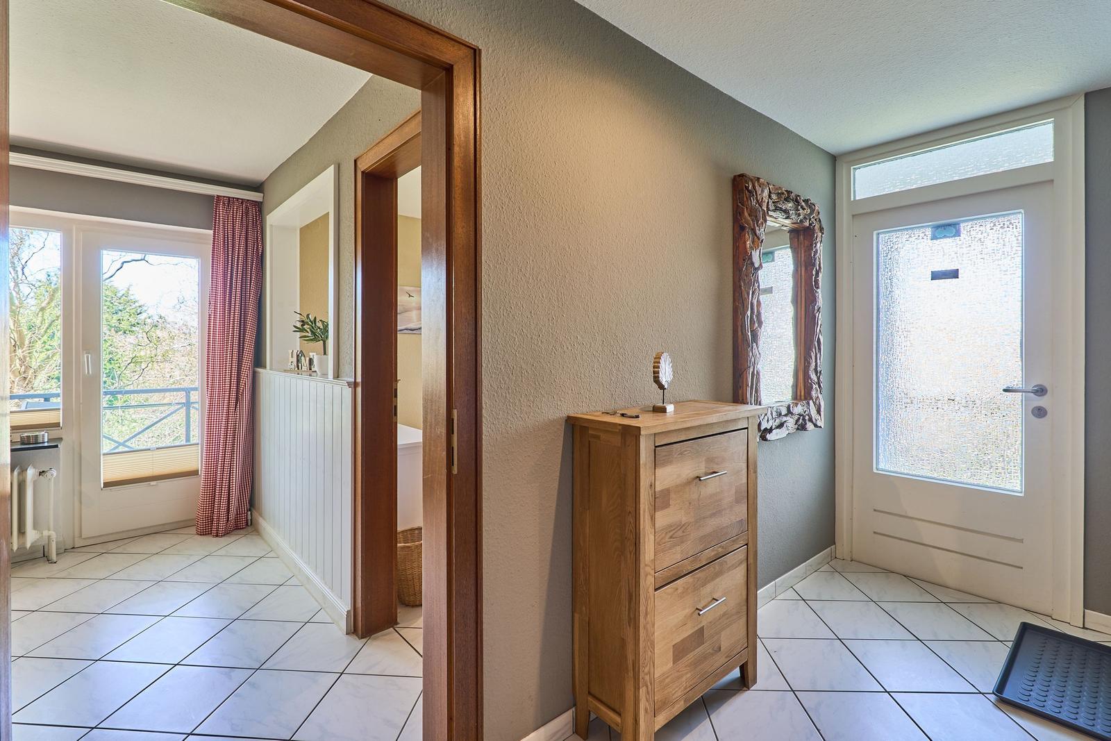 Eingangsbereich mit Holzschrank, Spiegel und Tür zum Balkon.