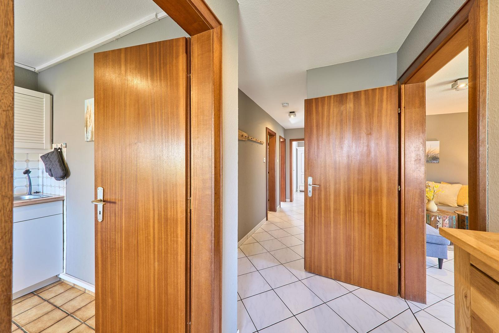 Hausgang mit Holztüren, Fliesenboden und Blick in Küche und Wohnzimmer.