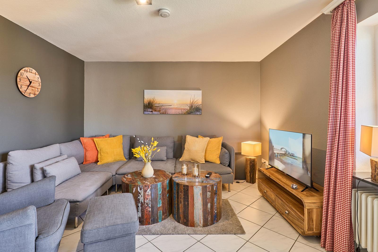 Ein Wohnzimmer mit grauem Sofa, zwei runden Tischen und einem Fernseher auf Holzregal.