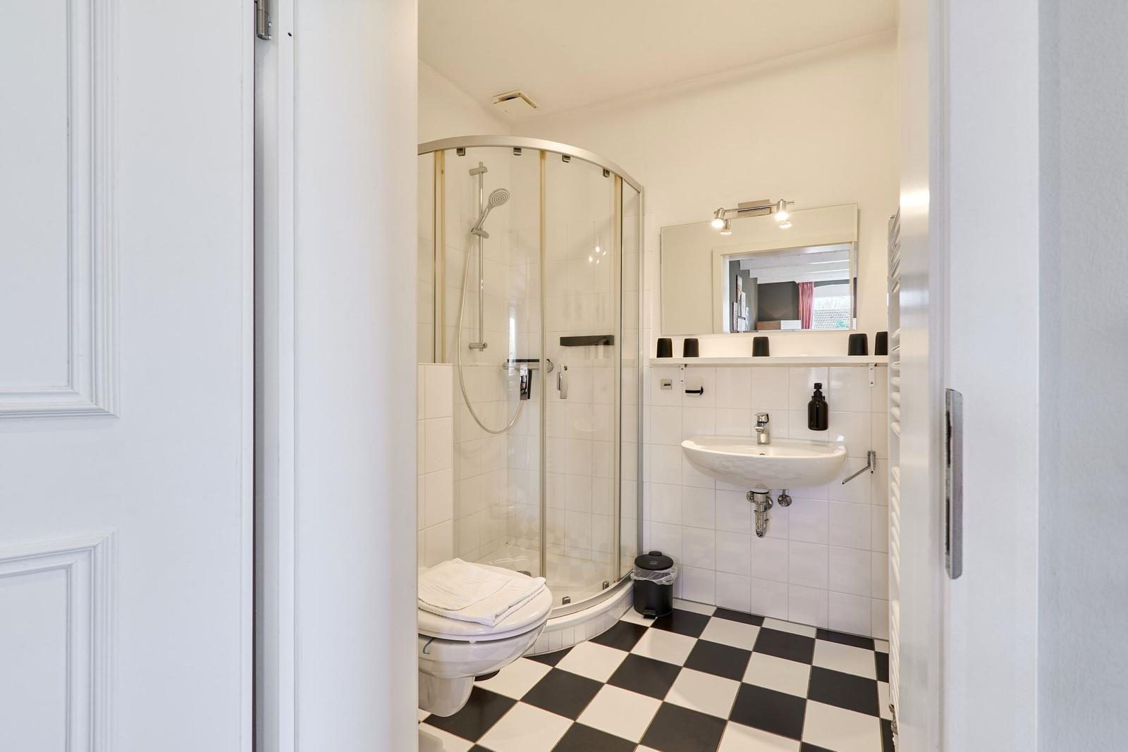 Badezimmer mit Dusche, Waschbecken und Toilette auf schwarz-weißem Fliesenboden.