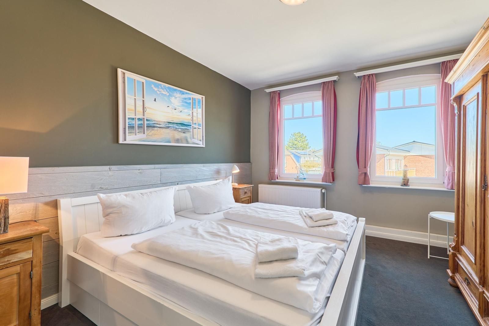 Schlafzimmer mit Doppelbett, zwei Fenstern und Holzmöbeln.